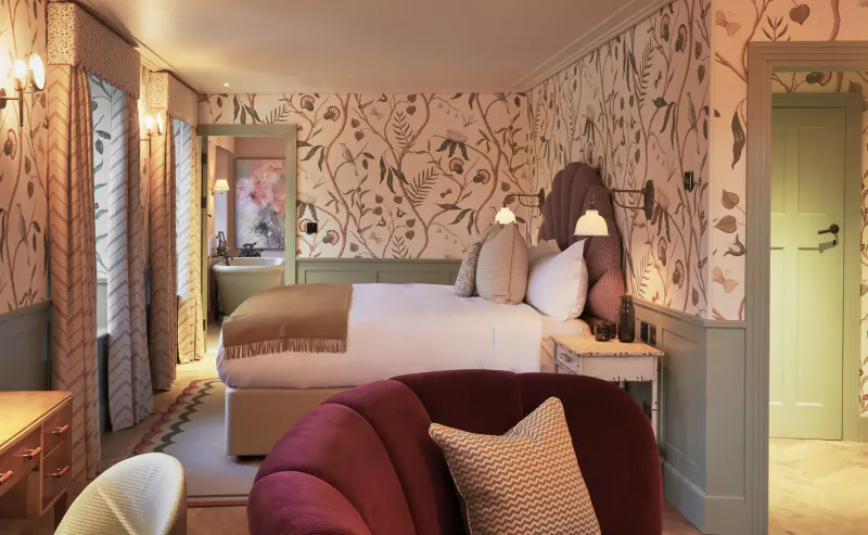Elegant bedroom in luxury retreat with floral wallpaper, king bed, velvet armchair, and soft lighting.
