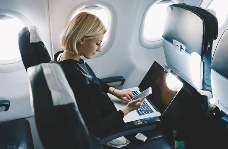 Blonde businesswoman working on laptop and phone in airplane seat on private jet