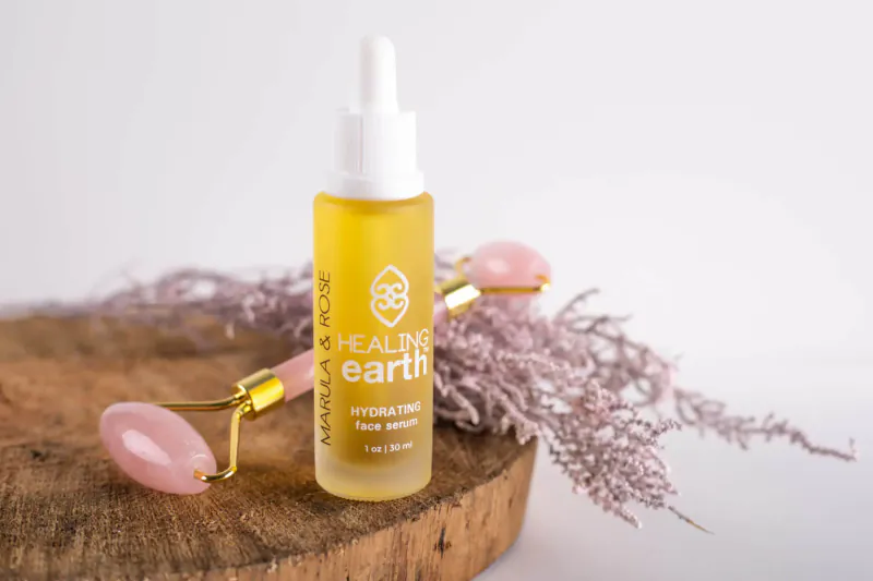 Healing Earth Hydro Tree Oil dropper bottle with rose quartz roller on wooden base amid purple fronds