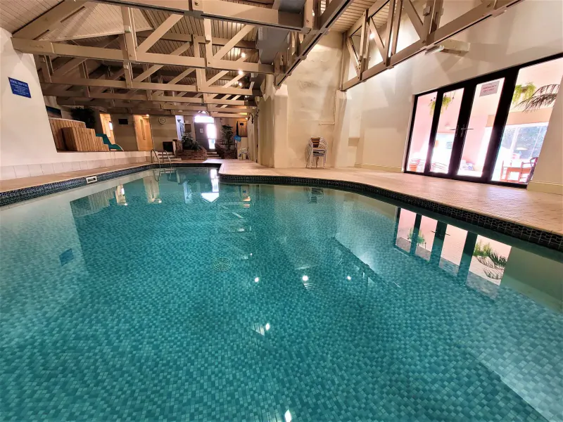 Indoor swimming pool at Broomhill Manor with turquoise water, wooden beamed ceiling, and large windows.