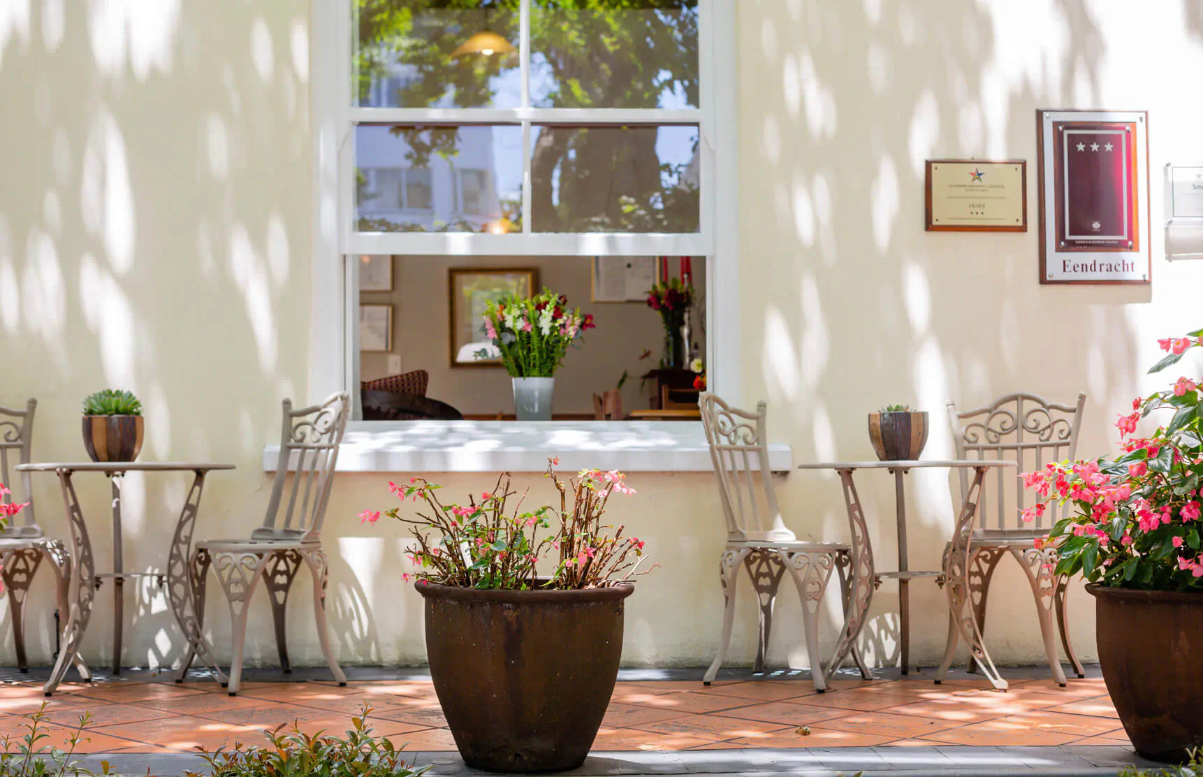 Outdoor café at Eendracht Hotel with ornate metal tables, chairs, potted flowers, and window view of interior bouquet.