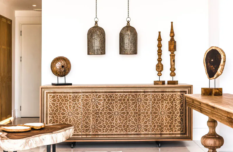 Elegant Moroccan-style room with carved wood buffet cabinet, hanging lanterns, wooden sculptures, and side tables.