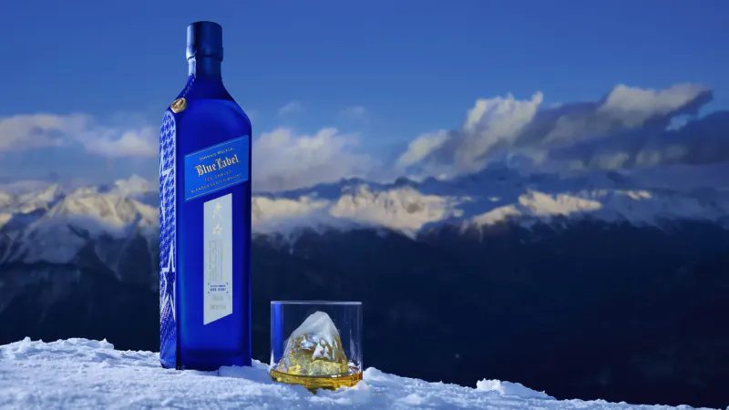 Johnnie Walker Blue Label bottle and whisky glass on snow with snowy mountains backdrop