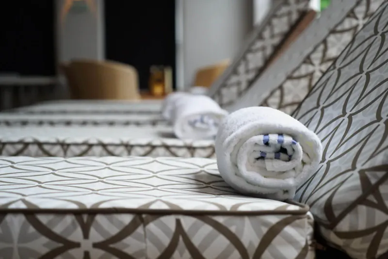 Close-up of white towels rolled on beige patterned lounge beds in a spa relaxation area.