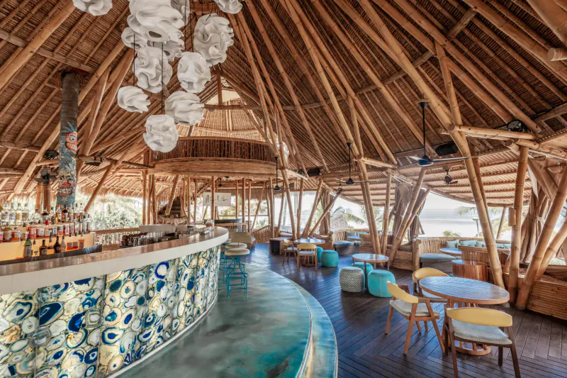 Azul Beach Club Bali: Tropical bamboo bar with blue peacock tile counter, pendant lights, colorful seating, ocean view.
