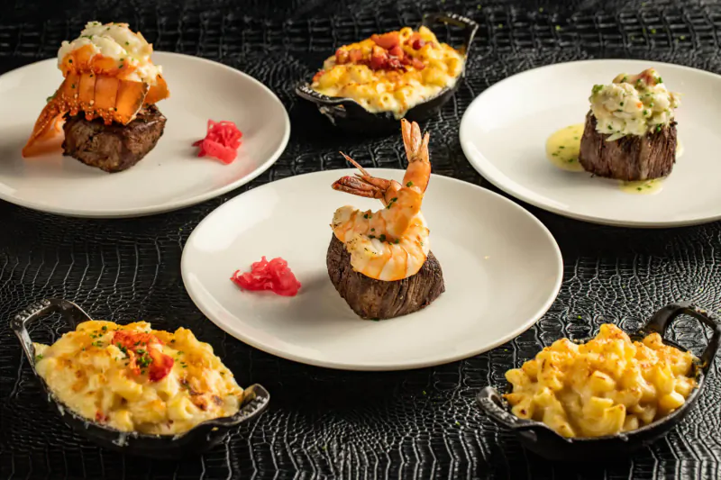 STK restaurant platter: seared steaks topped with lobster and shrimp, mac and cheese in skillets, garnished with red seaweed.
