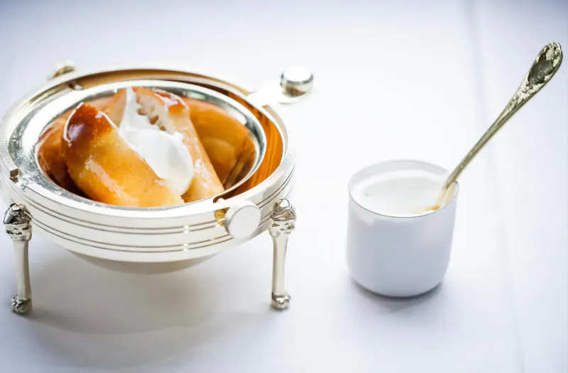 Elegant silver pedestal bowl of pears with cream, beside white creamer and spoon on white tablecloth