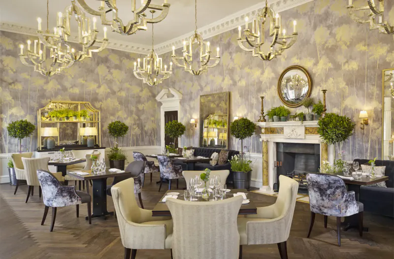 Elegant dining room at The Langley luxury hotel with floral wallpaper, chandeliers, plants, and tables set for meals.