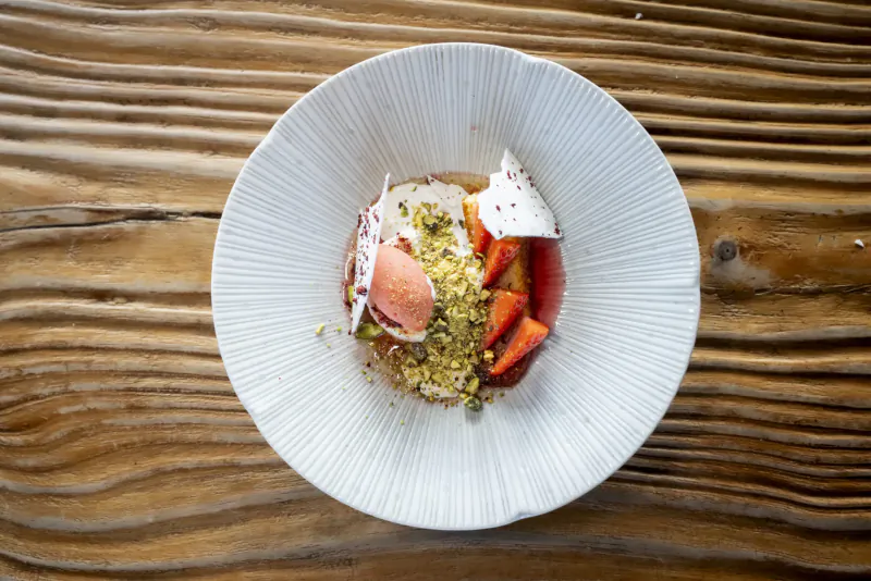 White plate on wooden table with strawberry sorbet, pistachios, fresh strawberries, and white meringue