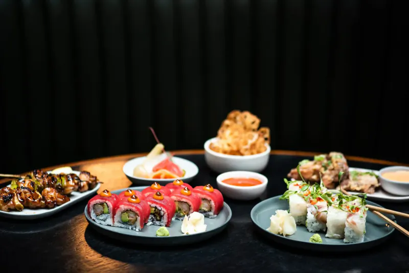 Assortment of sushi rolls, yakitori skewers, spring rolls, and crispy snacks on plates at Apothecary East tavern.