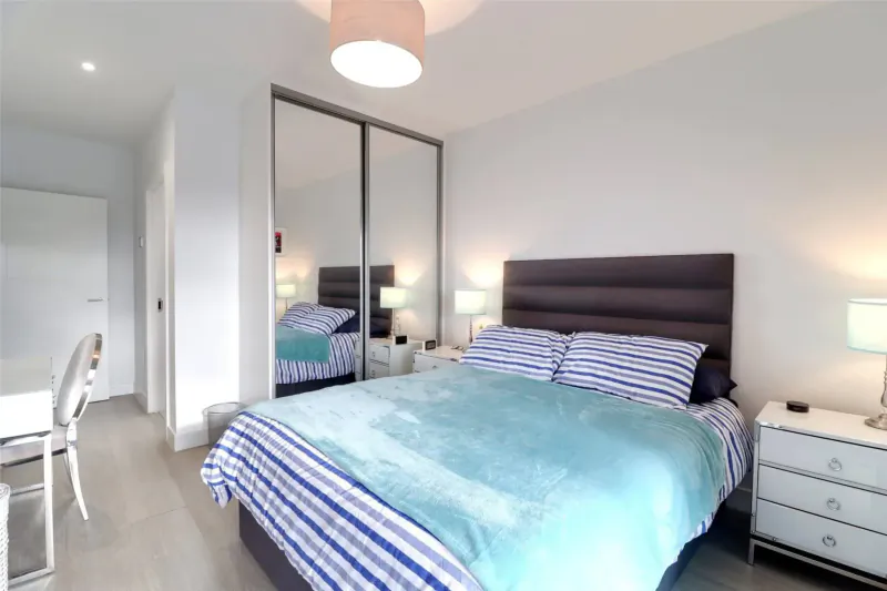 Bright modern bedroom with turquoise quilt on king bed, white desk, mirrored wardrobe, lamps, in Woolacombe Bay stay.
