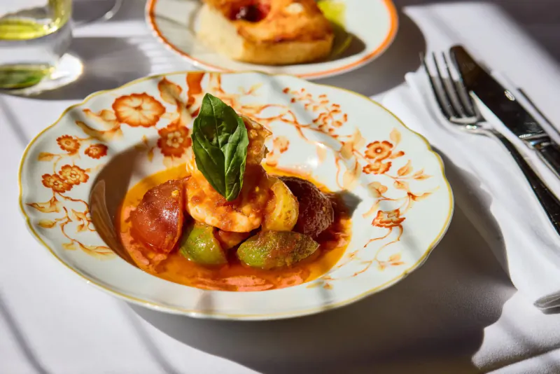 Close-up of shrimp with chorizo and olives in orange sauce, garnished with basil, in ornate bowl on restaurant table