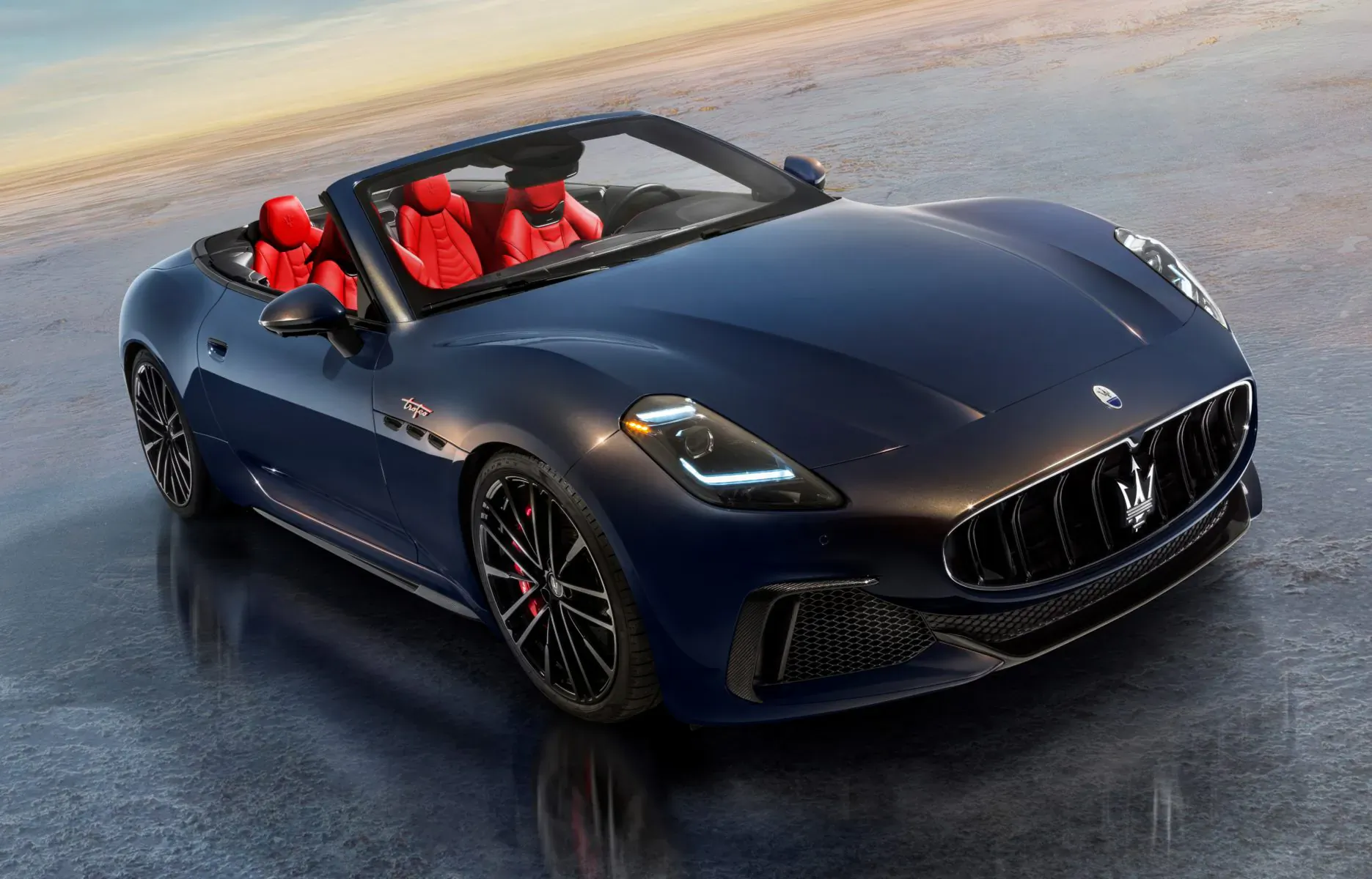 New Maserati GranCabrio Spyder in navy blue with red leather seats, front view at sunset on reflective surface