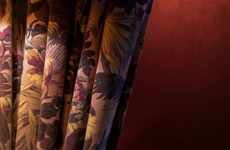 Close-up of ornate floral curtains in warm lighting at House of Gods Hotel, Edinburgh, against red wall.