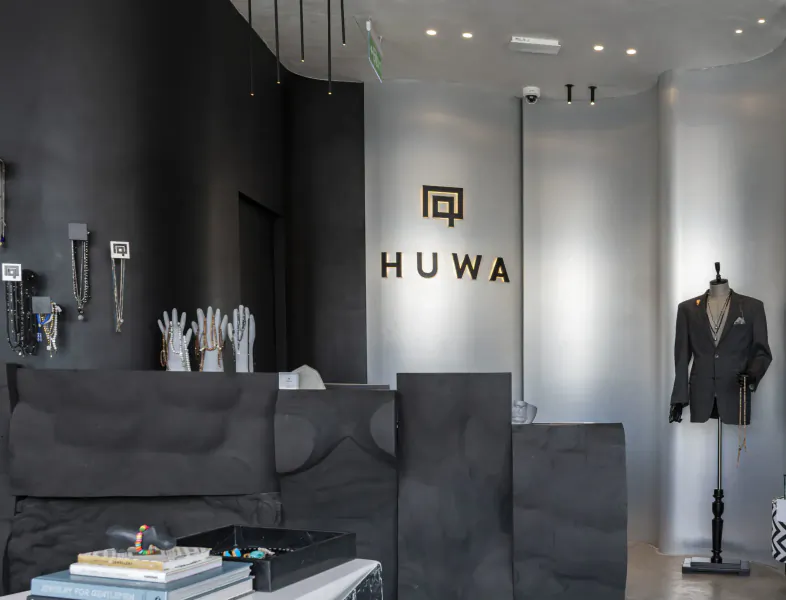Modern Huwa men's jewellery flagship store interior in Cairo with black suit on mannequin, white gloves, reception desk, and logo.