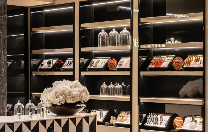 Luxurious hotel boutique display with glass shelves of perfume bottles, cosmetics, and white floral centerpiece.