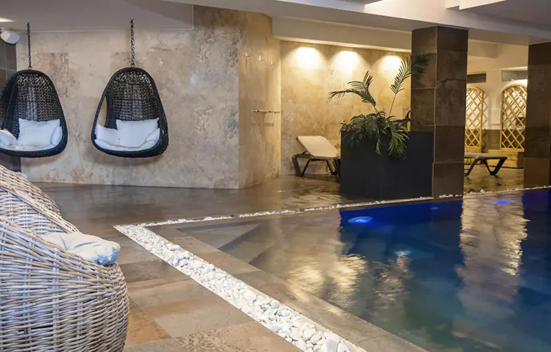 Luxurious spa poolside with white hanging egg chairs, loungers, plants, and warm lighting at Village Boutique & Spa.