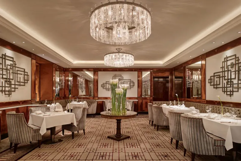 Elegant dining room in Hotel Imperial Vienna with crystal chandeliers, round table with calla lilies, and geometric wall art.