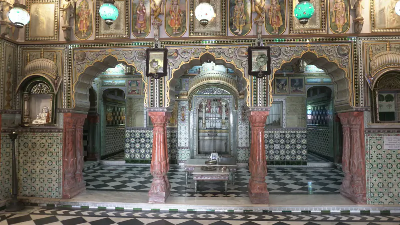 Ornate interior of a Rajasthan haveli with red sandstone arches, green lamps, intricate tilework, and checkered marble floor.
