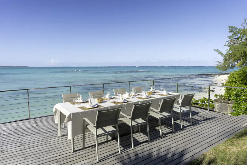Elegant long white-clothed dining table set on wooden deck overlooking turquoise ocean at Villa Ruby, Belle Mare, Mauritius