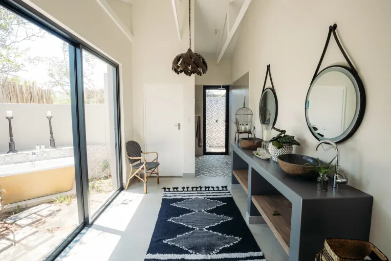 Bright hallway in luxury safari lodge with sliding doors to pool, rattan chair, woven rug, pendant light, and vanity mirror.