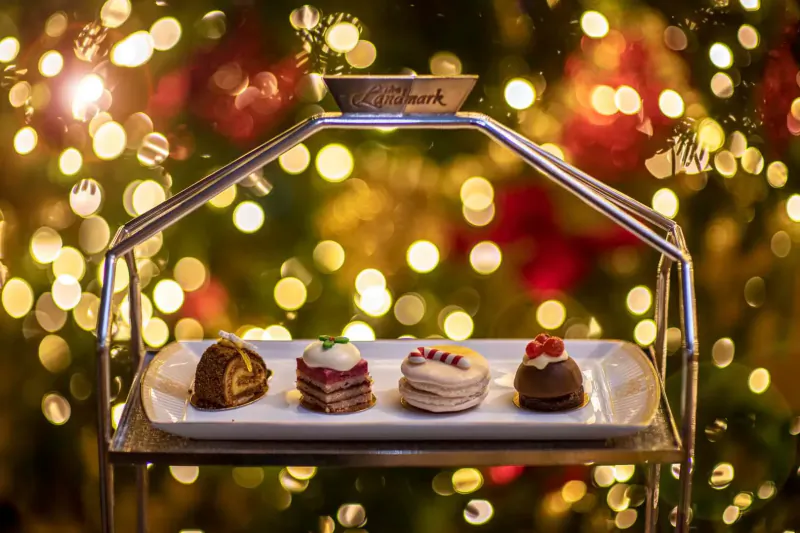 Elegant tiered stand with four Christmas pastries: roll, cake, macaron, chocolate, against festive bokeh lights