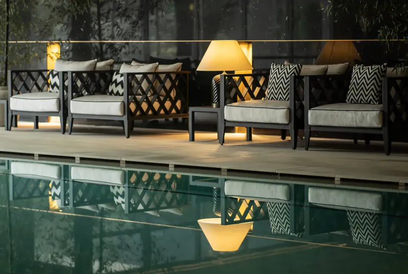 Elegant black lounge chairs with cushions and lamps beside a lit pool at night, reflecting in water, Vinha Boutique Hotel.