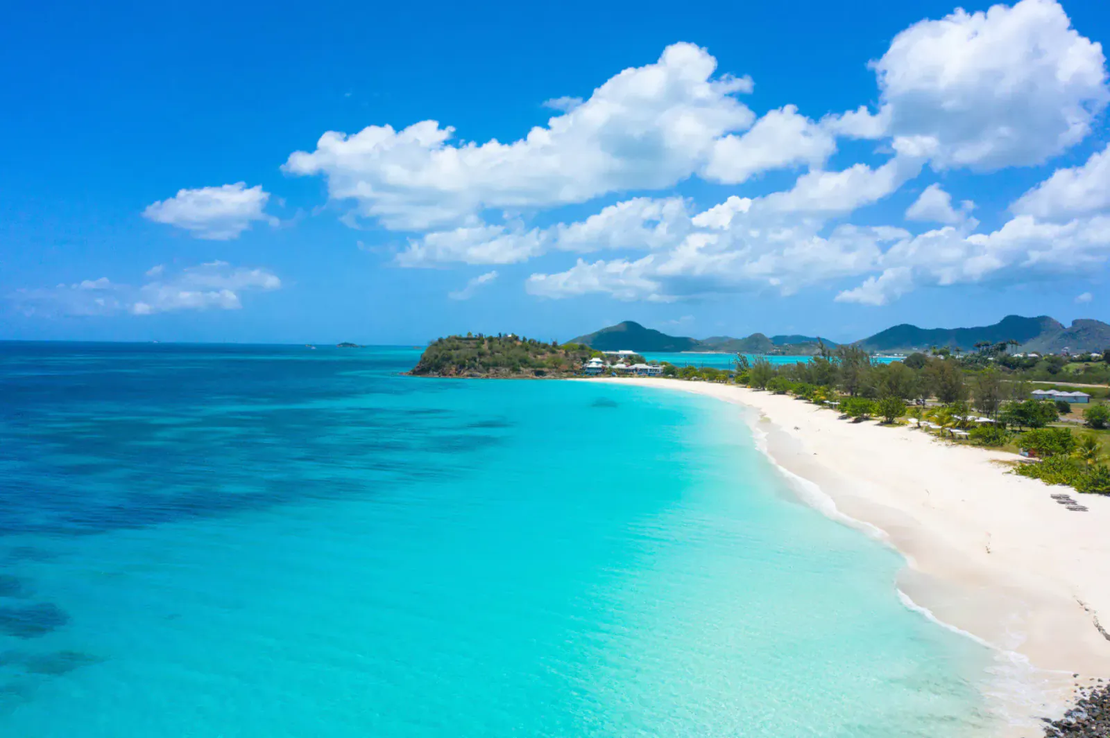 Aerial view of white sand beach and turquoise Caribbean sea in Antigua and Barbuda under blue sky with clouds.