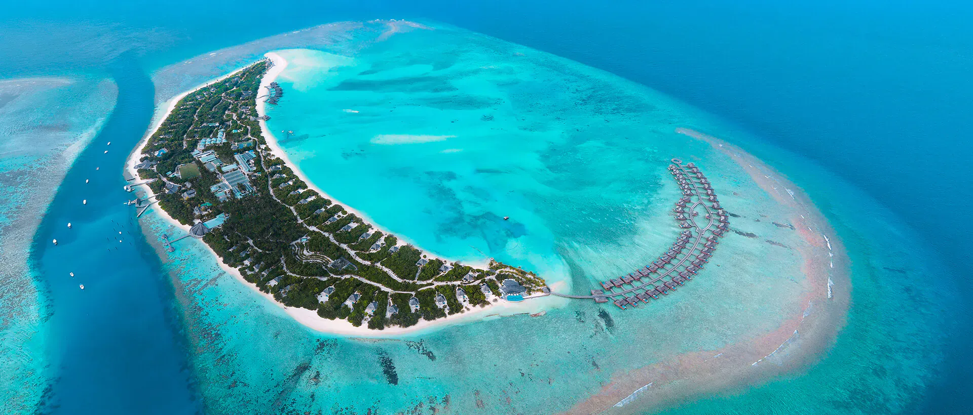 Aerial view of Hideaway Beach Resort & Spa, luxurious villas on a lush tropical island with turquoise lagoon and white sand beaches.