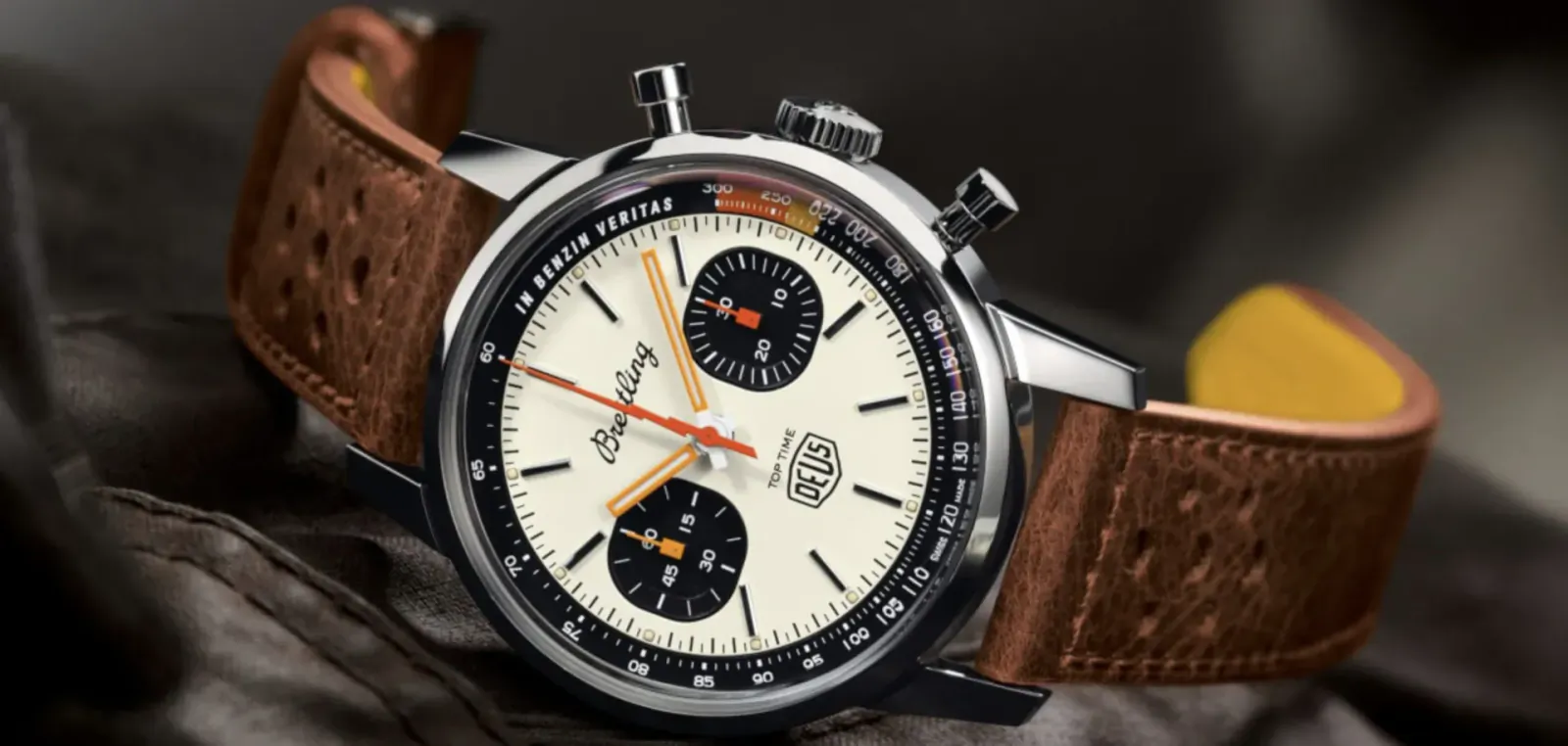 Breitling Top Time Deus Limited Edition chronograph watch with white dial, black subdials, orange accents, and brown leather strap on dark surface.