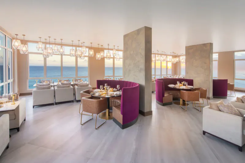 O2 Beach Club & Spa: Luxurious dining lounge with purple velvet booths, ocean sunset views, chandeliers.