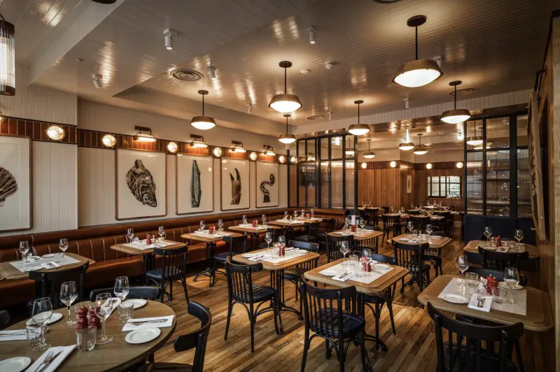 Elegant restaurant interior at Battersea Power Station with wooden tables set for dinner, pendant lights, and large leaf art on walls.