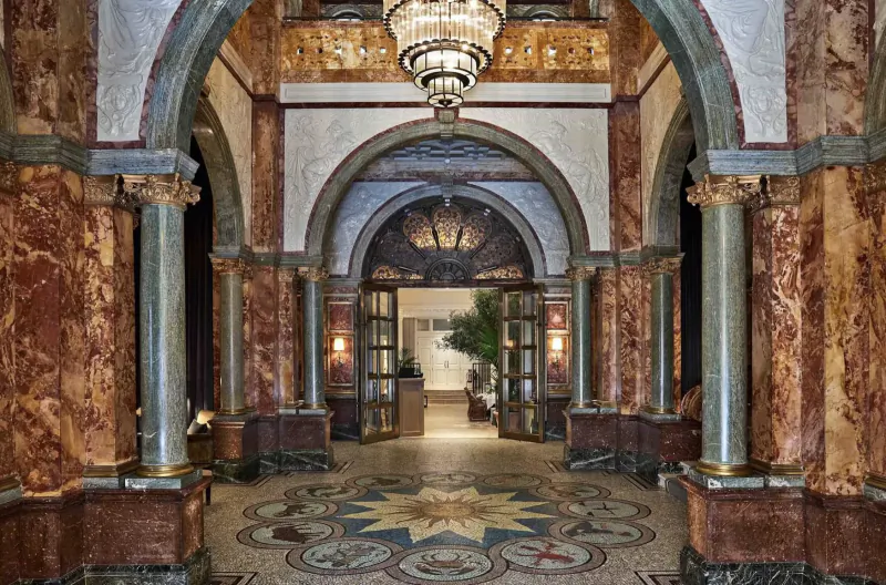 Grand arched entrance hall of Kimpton Fitzroy London with chandelier, marble columns, and ornate mosaic floor.