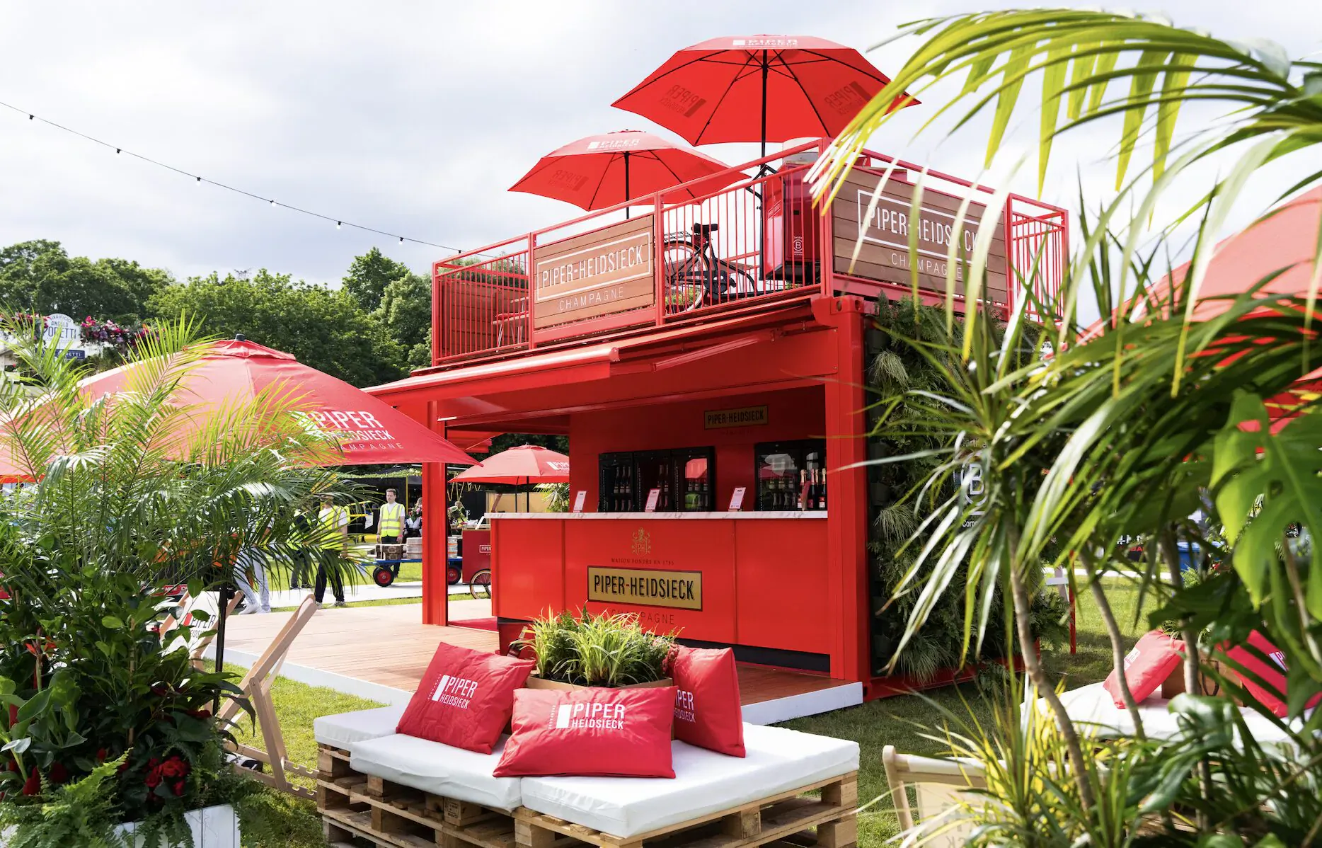 Piper-Heidsieck red Champagne Garden at Taste of London with bar, red umbrellas, lounge seating, palms, and people.
