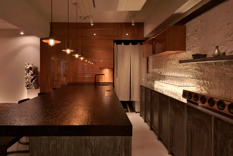 Stylish contemporary restaurant interior with wooden bar counter, pendant lights, glassware, and brick walls.