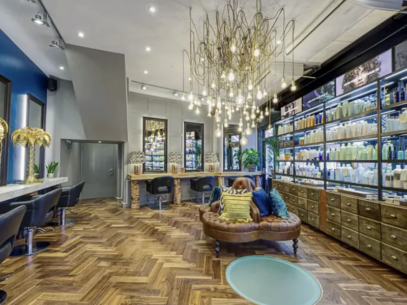 Edward Charles modern hair salon interior with wooden floors, black chairs, product shelves, and chandelier.