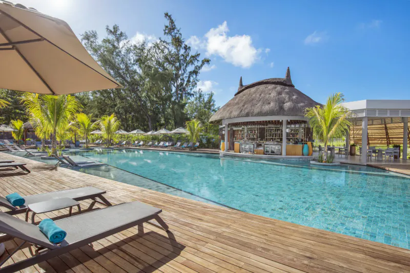 Infinity pool deck with loungers and towels at Anantara Iko Mauritius resort, thatched bar, palms, blue sky.