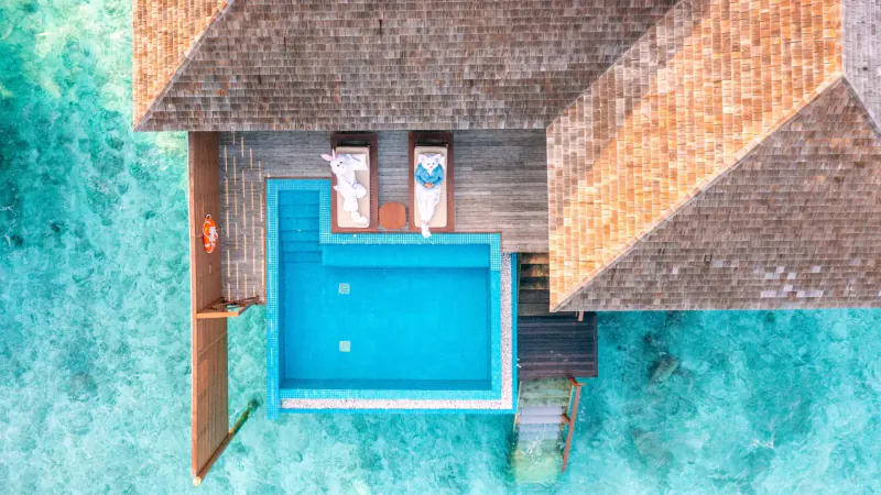Aerial view of luxury overwater villa with infinity pool, lounge chairs, and turquoise lagoon