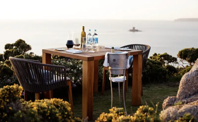 Elegant outdoor table set with wine bottle, water bottles, ice bucket, and glasses overlooking sunset sea view at PoB Hotels.