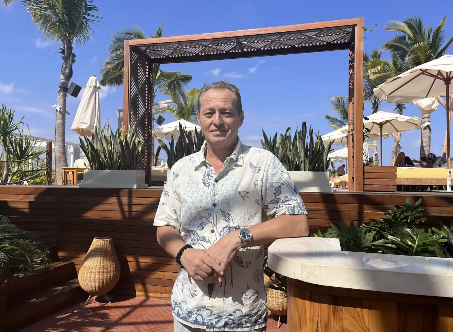 Sylvain Croise, GM of Secana Beachtown Bali, smiling in white floral shirt at tropical beach resort poolside