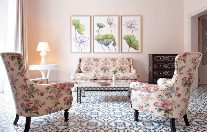 Cozy hotel lounge with floral-upholstered armchairs and loveseat around glass coffee table, lotus flower art on pink wall.