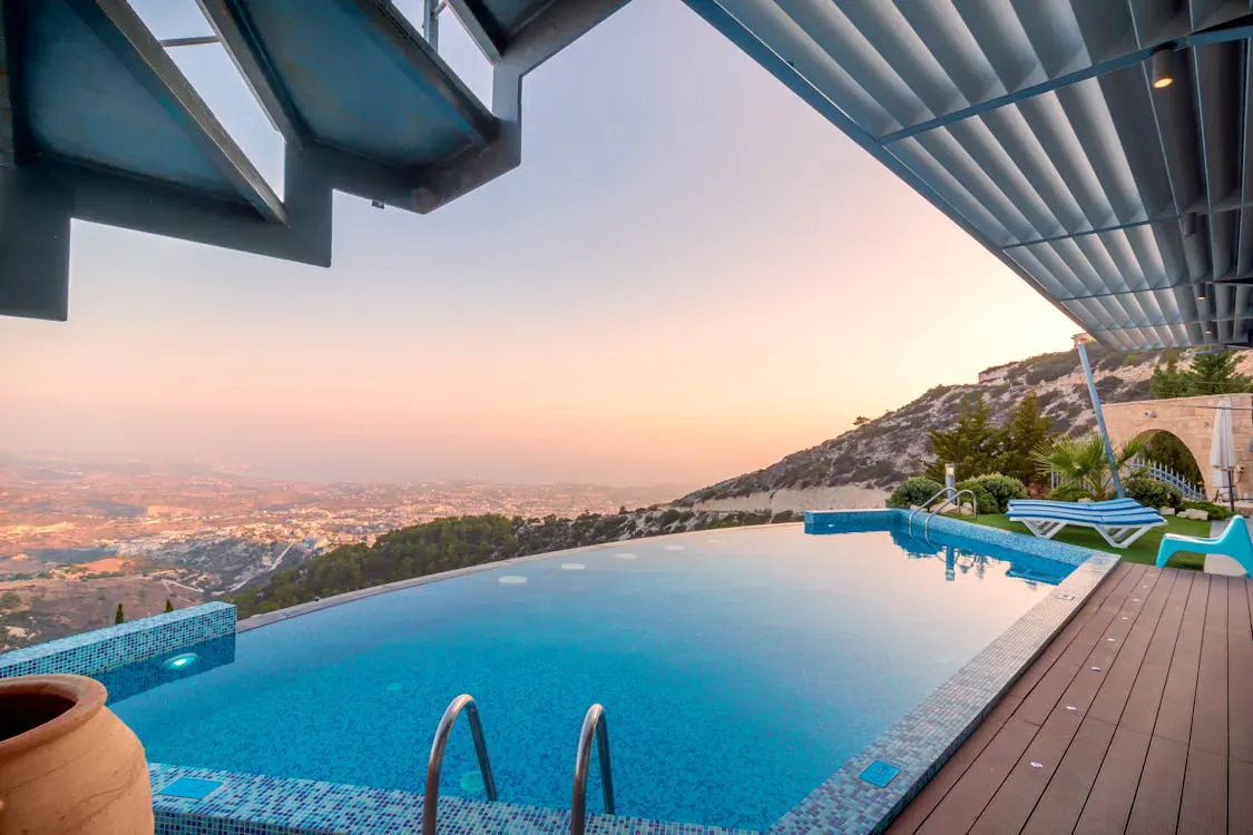 Infinity pool on a luxurious deck overlooking sunset cityscape and hills from a modern villa