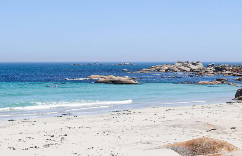Sandy beach with turquoise waves lapping rocks at Paternoster under clear blue sky