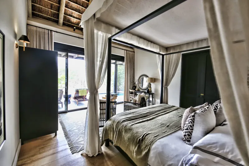 Luxurious bedroom at Monwana Game Lodge with four-poster bed, open doors to patio and pool overlooking bushveld.
