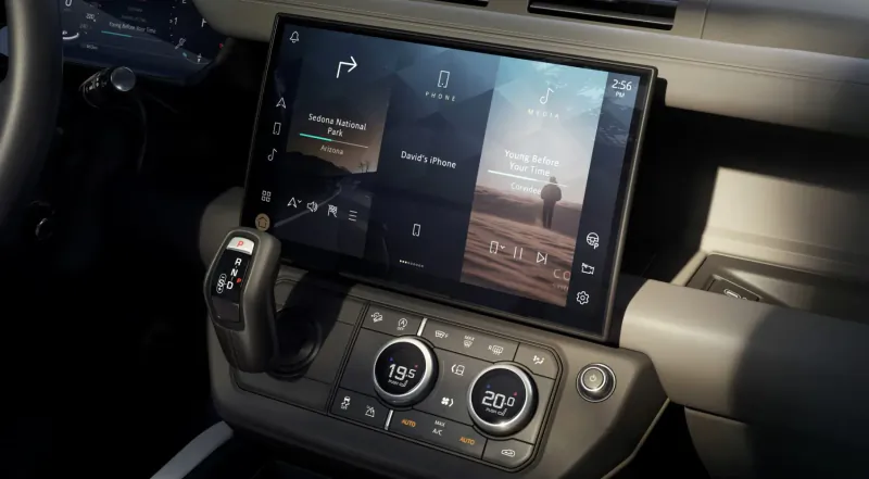 Land Rover Defender dashboard with central touchscreen displaying 'South Place' and desert scene, gear selector, and controls.