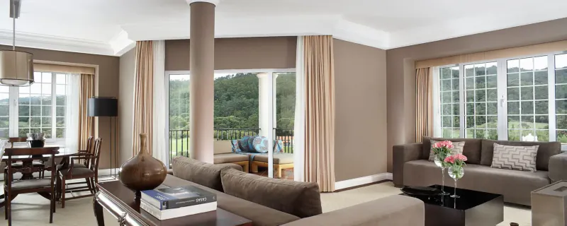 Spacious luxury suite at Penha Longa Resort with beige sofas, dining table, and panoramic golf course views through large windows.