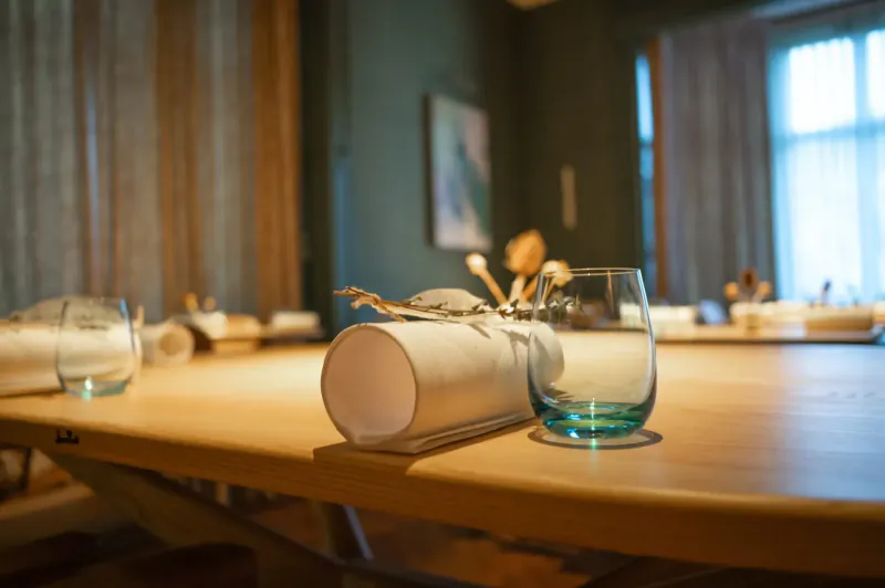 Close-up of wooden table with rolled napkins, clear glasses, wooden spoons, and dried flowers in elegant dining room.