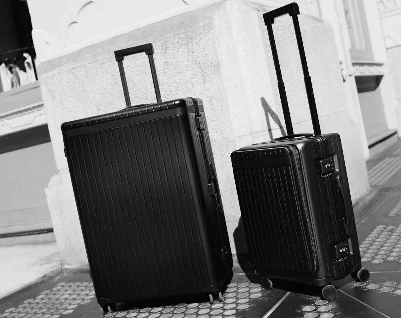 Two black Carl Friedrik rolling suitcases, large and medium, side by side on pavement.