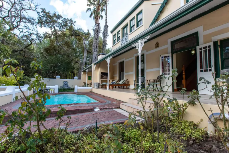 Evergreen Manor and Spa in Stellenbosch: yellow house with green trim, veranda, pool, palms, and gardens