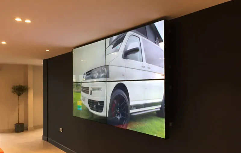 Large video wall displaying white camper van on green field in modern office with dark walls
